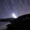 Imagem do rasto da Lua a pôr-se por trás da Serra da Arrábida. São visíveis várias estrelas das constelações: Andrómeda, Peixes, Baleia, Carneiro, Cassiopeia à direita e ao centro no topo, as Plêiades.