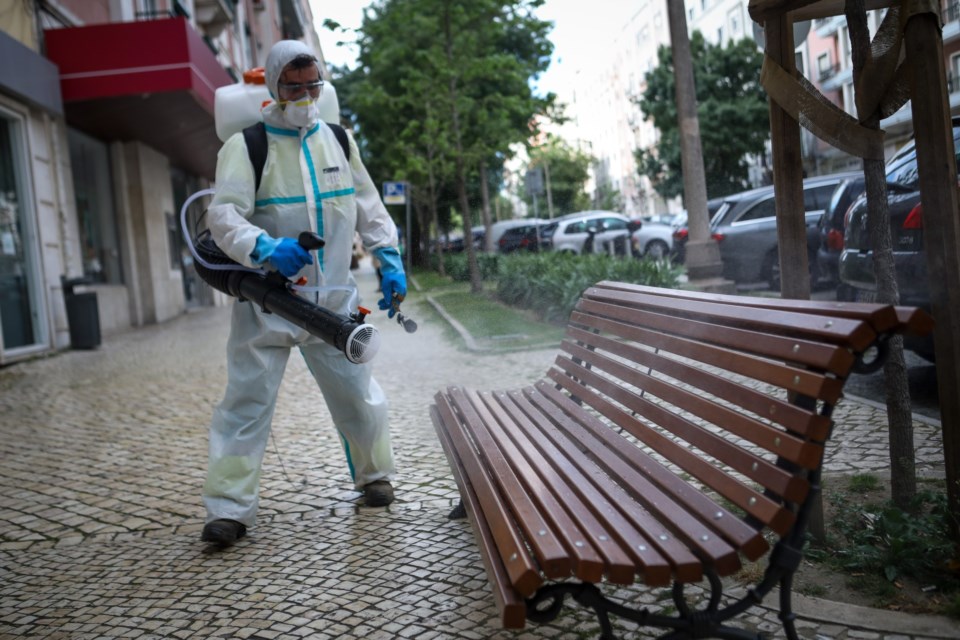 Homem em fato de proteção completo desinfeta um banco de jardim num espaço público em Lisboa.