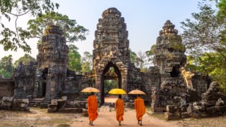 Three buddhist monks with umbrellas, walking inside Angkor Wat temple. Siem Reap, Cambodia