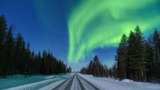 Scenic sky with Northern Lights over an empty snowy road into a forest, Levi, Kittila, Lapland, Finland�