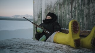 Barentsburg, Svalbard, Noruega. Uma mulher sentada no exterior segura uma arma que serve para afugentar ursos polares.