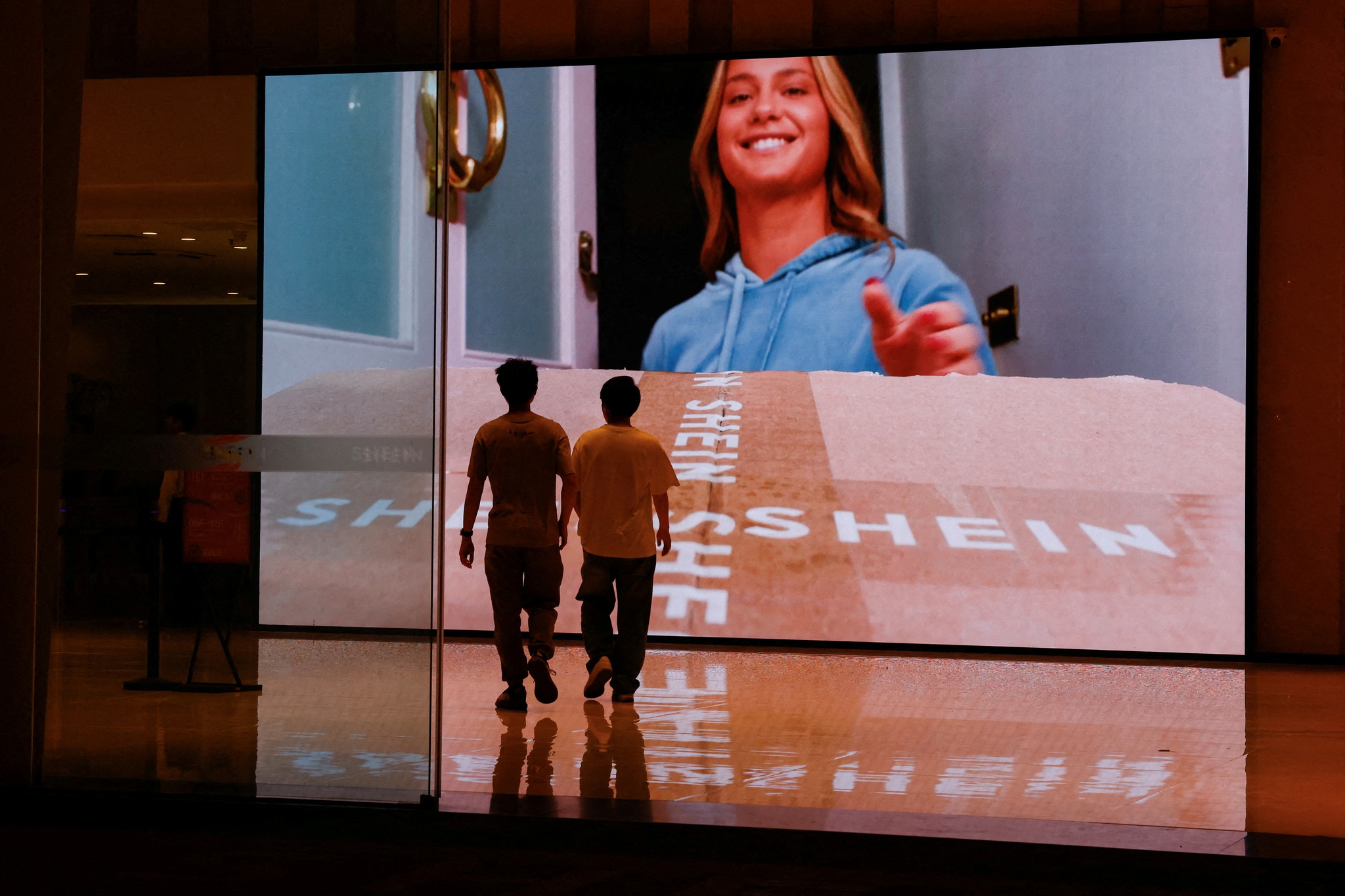 FILE PHOTO: People walk past a screen showing a promotional video of Shein at the company's office building in Guangzhou, Guangdong province, China April 16, 2025. REUTERS/Tingshu Wang/File Photo