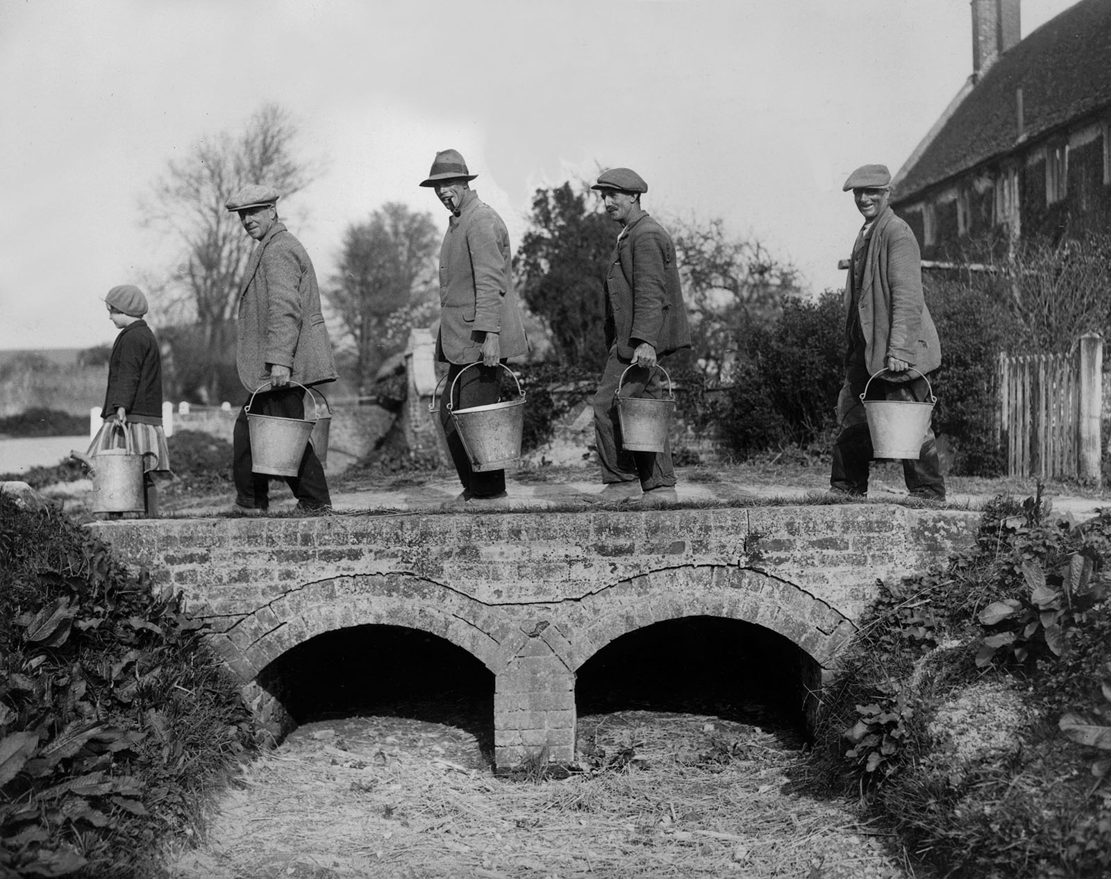 2nd May 1934:  Villagers of Imber in Wiltshire returning home with water drawn from one of the village's only remaining wells. The spring over which they are walking is by now completely dry, and if the two wells dry up also, the villagers will have to be evacuated.  (Photo by William Vanderson/Fox Photos/Getty Images)