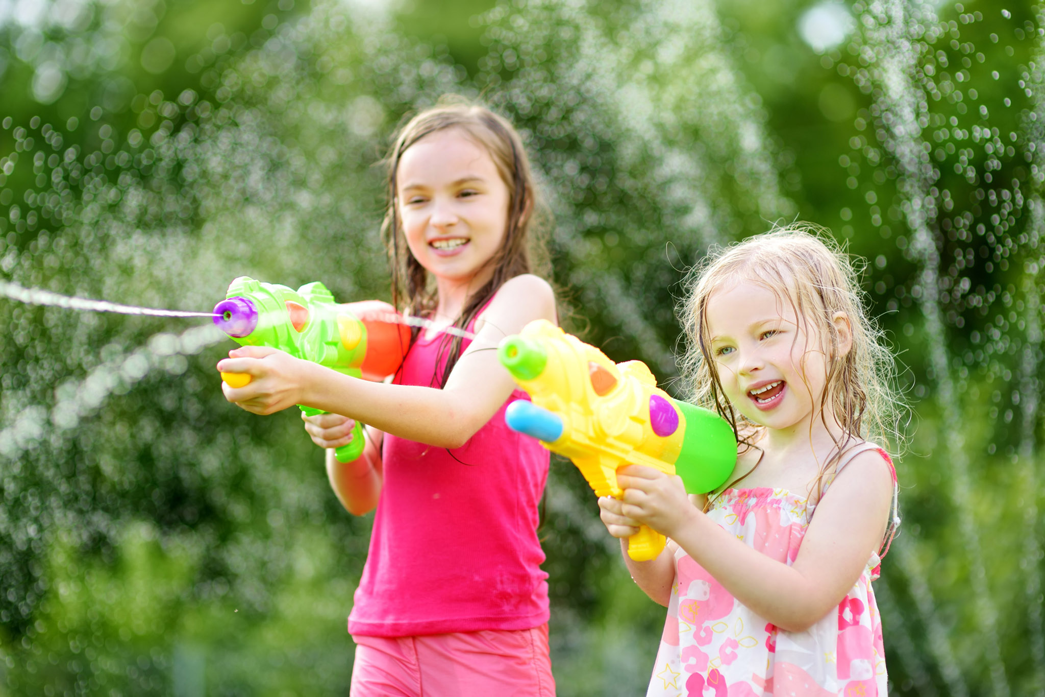 Adorable little girls playing with water guns on hot summer day. Cute children having fun with water outdoors.