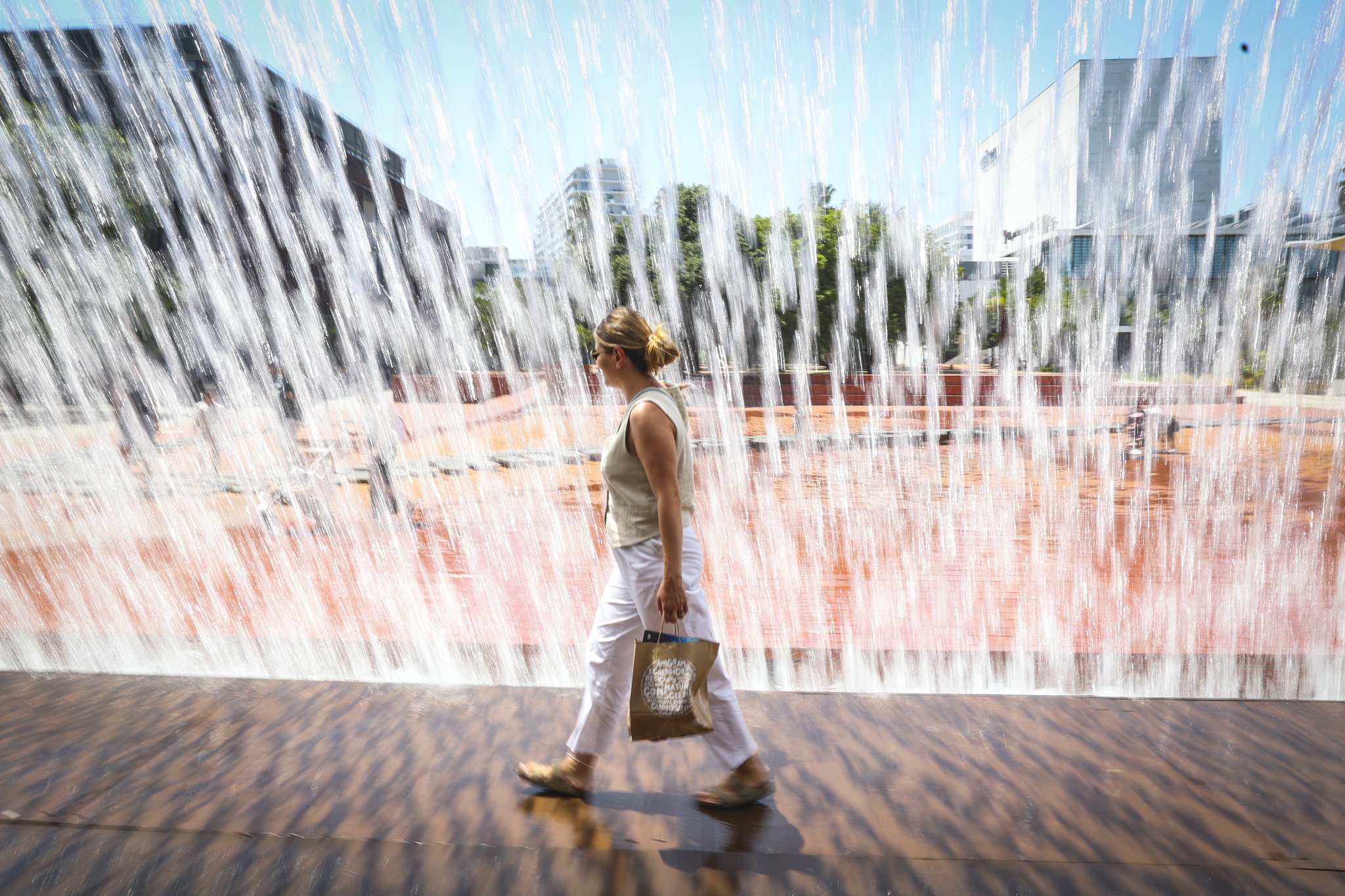 epa13083555 A woman walks beside a fountain in Lisbon, Portugal, 03 July 2026. The Portuguese weather agency (IPMA) issued red alerts as extreme heat affected parts of the country. EPA/ANTONIO PEDRO SANTOS